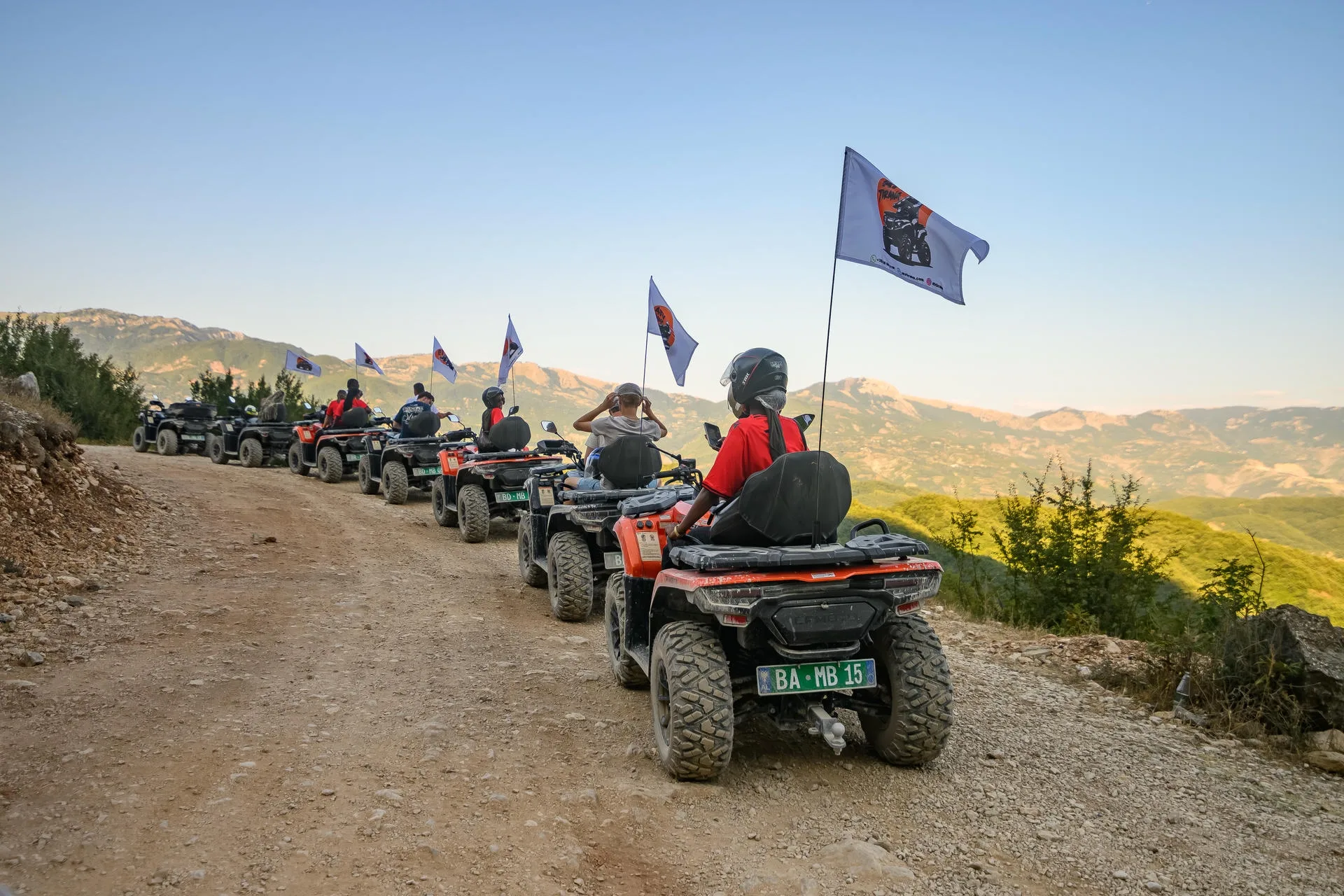 A long ATV Tirana quad convoy approaching the Bovilla Lake viewpoint with branded flags