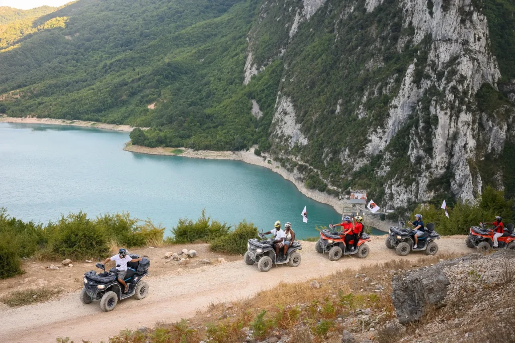 An ATV Tirana quad convoy riding along the mountain track above turquoise Bovilla Lake