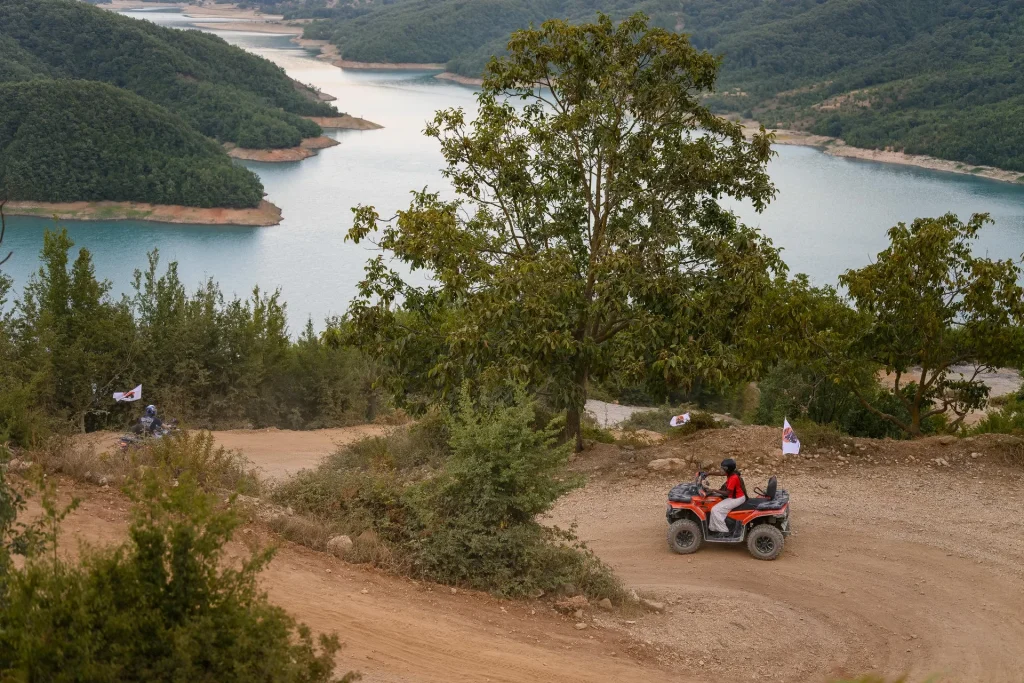 A quad rider rounding a wide dirt turn with Bovilla Lake visible through the trees