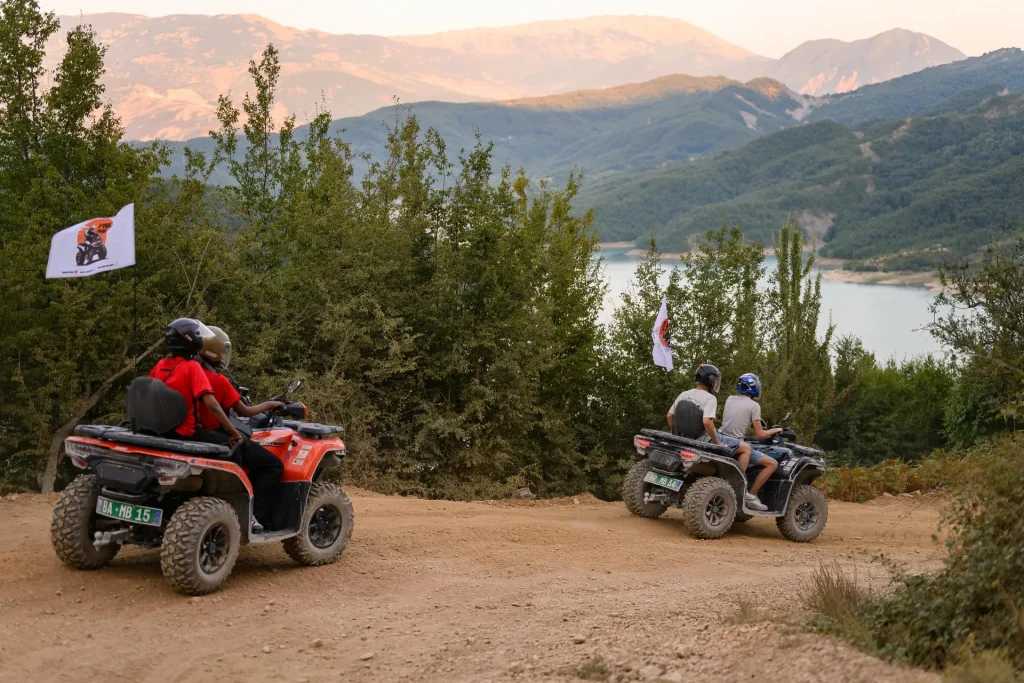 Two ATV Tirana quad bikes descending a dirt trail with Bovilla Lake behind them