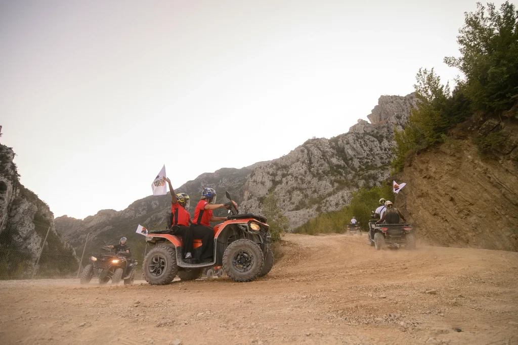 A red-shirted ATV Tirana rider accelerating through dust on an off-road trail