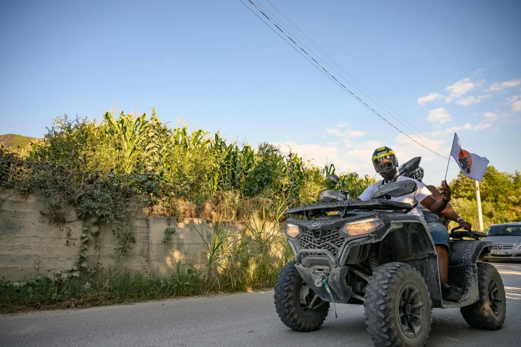 A helmeted ATV Tirana rider passing the camera on a quad bike with a branded tour flag