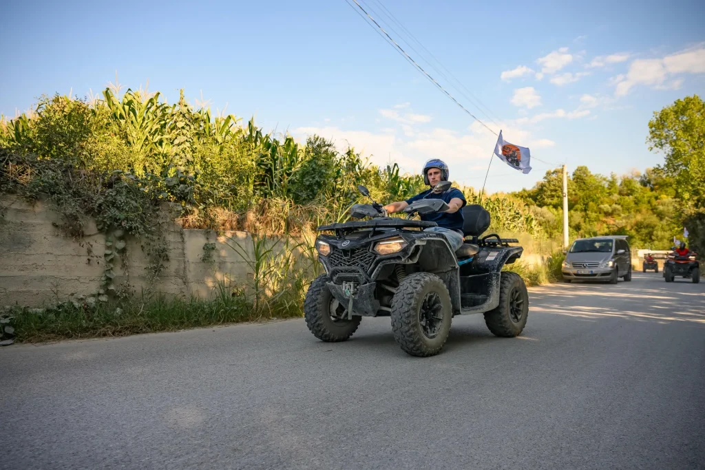 An ATV Tirana rider passing along a sunny village road on a guided quad tour