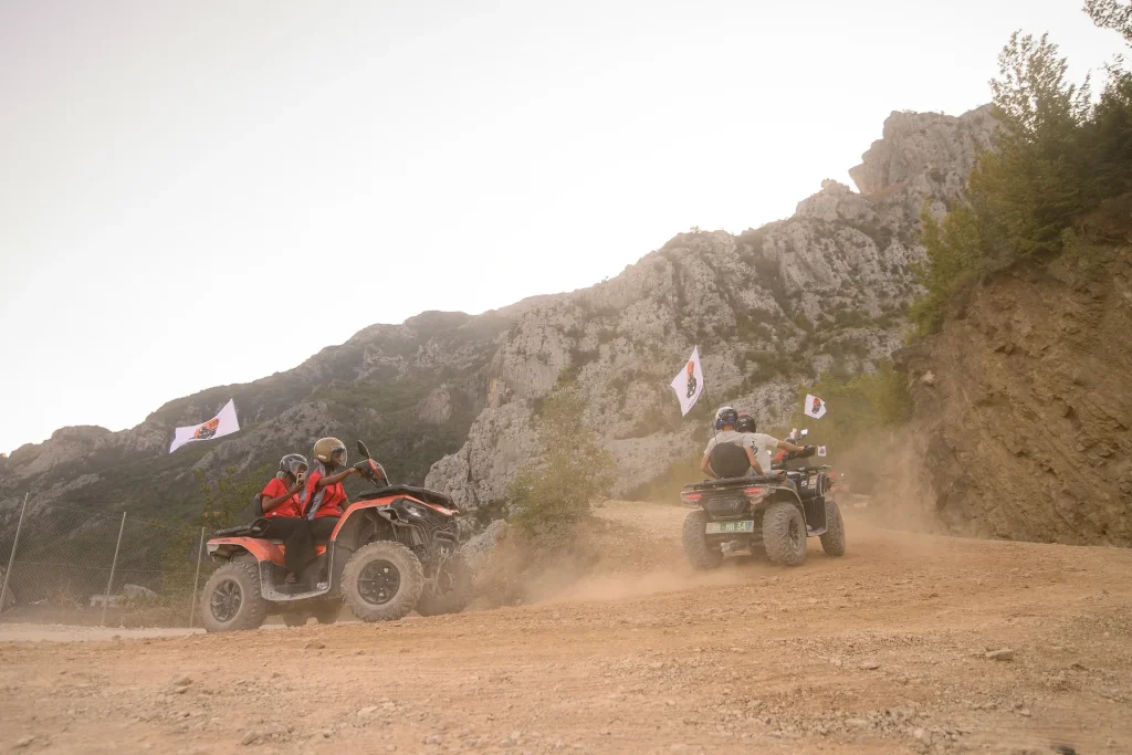 Two quad riders following each other across a dusty off-road section