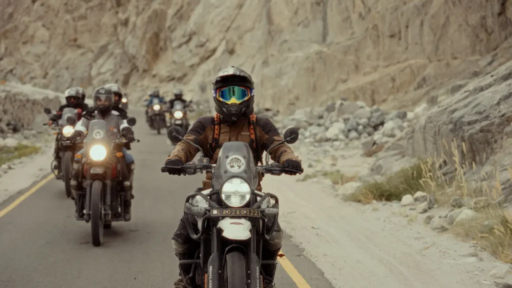 Illustrative adventure-motorcycle group riding through a rocky mountain valley