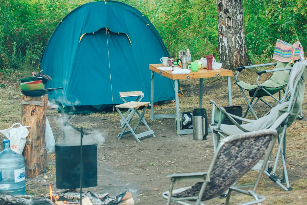 Illustrative campsite with a tent, chairs, cooking gear and a small campfire